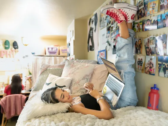 two female-identifying students in a dorm room looking content