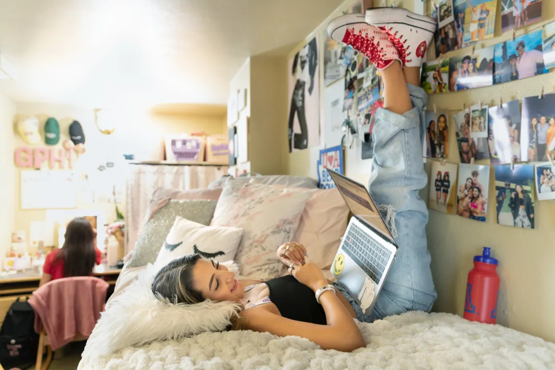 two female-identifying students in a dorm room looking content